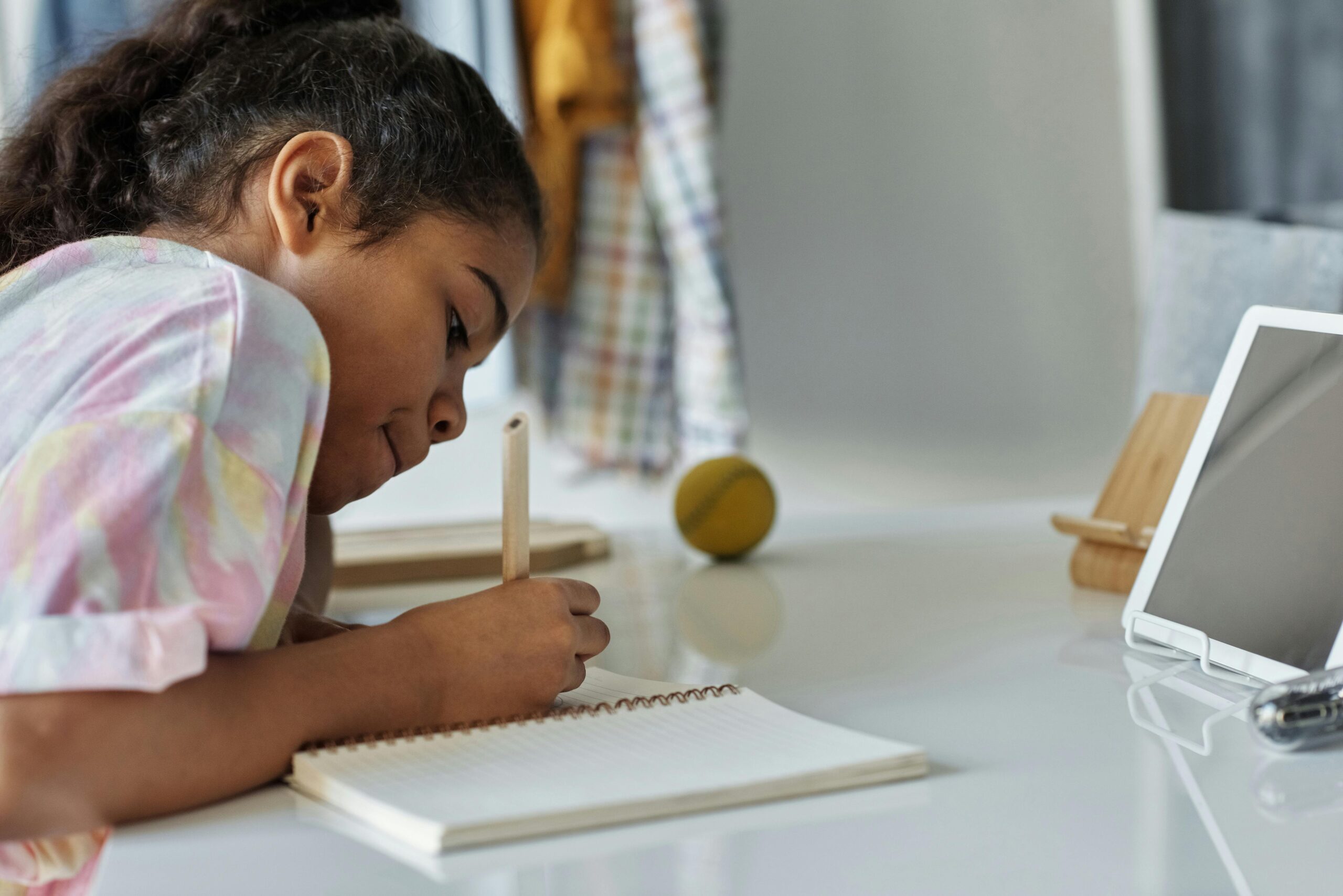 A young girl concentrating on homework at home using a tablet.