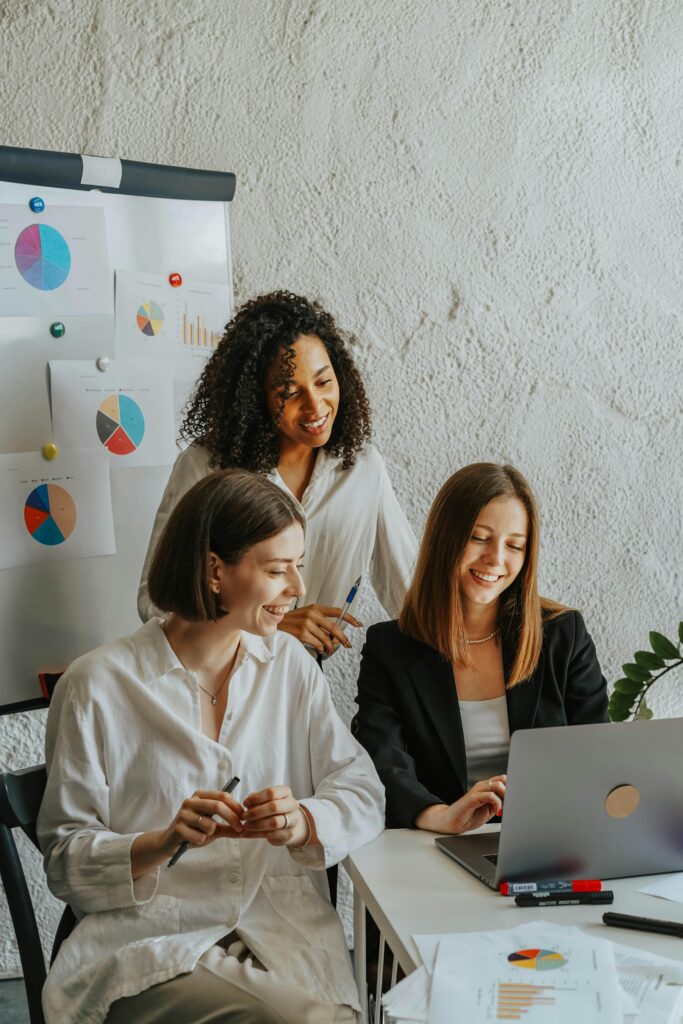 pexels-photo-8145247-8145247 Three businesswomen collaborate with graphs and a laptop in a modern office setting.